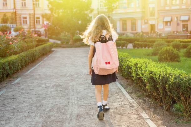 istock Rear view of young schoolgirl in uniform with backpack going to 975620720