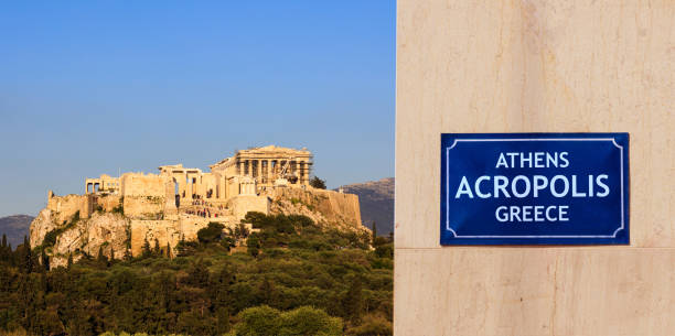 Greek flag on pole over classic building rooftop with blue sky in background