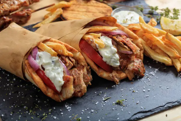 Greek gyros wrapped in pita breads on a black plate
