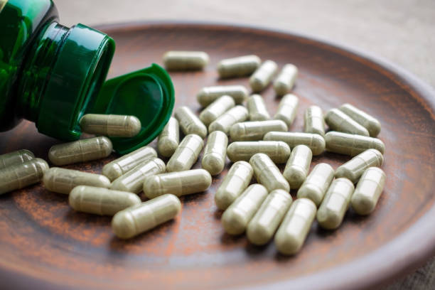 istock Close up green tea extract capsules and bottle on a clay brown plate on a burlap background 975647300
