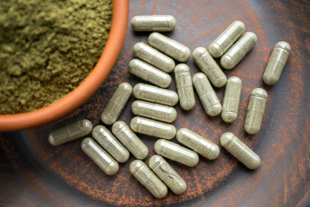 istock Close up Green capsules and powder on a clay brown plate on a burlap rustic background 975647342