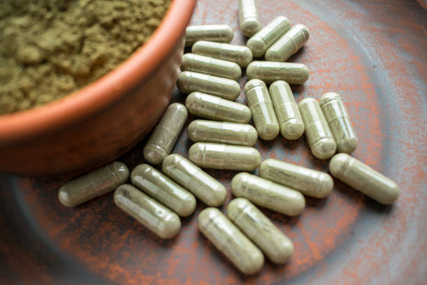 Supplement kratom green capsules and powder on brown plate Supplement kratom green capsules and powder on brown plate. Herbal product alt-medicine kratom is  opioid. Home alternative pain remedy, opioid addiction, dangerous painkiller, overdose. Close up. Selective focus morphine drug stock pictures, royalty-free photos & images