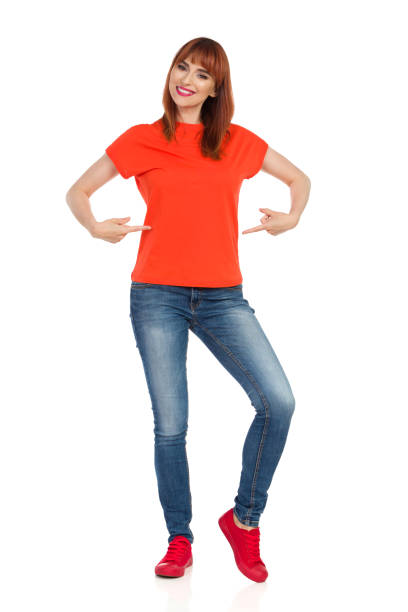istock Smiling Young Woman Is Pointing At Her Orange Shirt 975656432