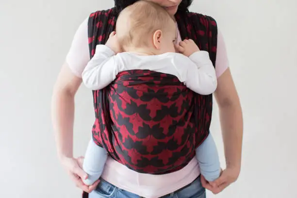 A front view of a babywearing mother carrying her small child in a sling.
