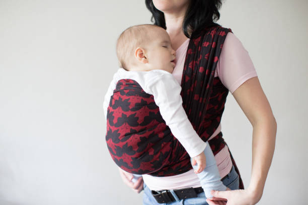 A babywearing mother carrying her sleeping child in a sling. stock photo