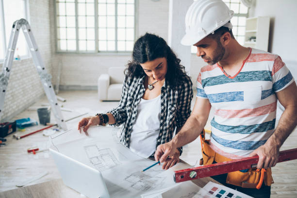 istock Young woman and construction worker looking at blueprints 975665854