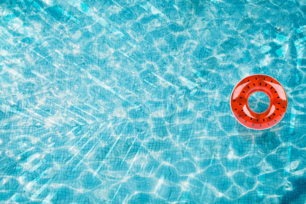 istock Pool floats, rings floating in a refreshing blue swimming pool with palm tree leaf shadows in water 975665896