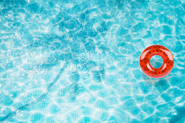 istock Pool floats, rings floating in a refreshing blue swimming pool with palm tree leaf shadows in water 975665900