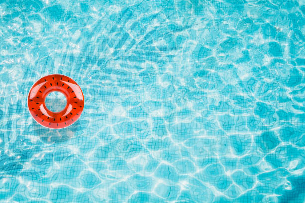 istock Pool floats, rings floating in a refreshing blue swimming pool with palm tree leaf shadows in water 975665918