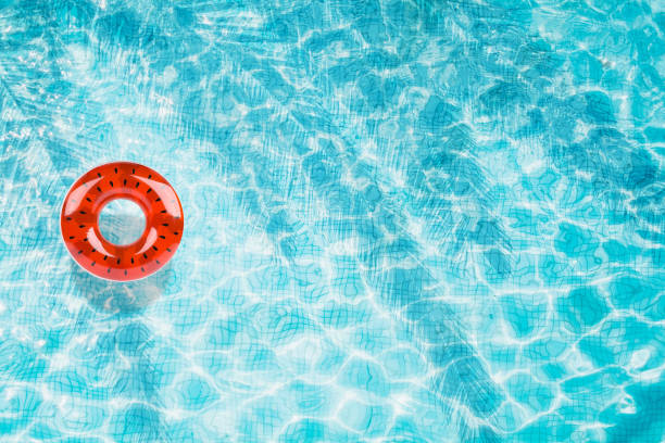istock Pool floats, rings floating in a refreshing blue swimming pool with palm tree leaf shadows in water 975665942