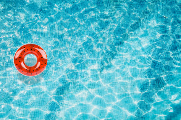 istock Pool floats, rings floating in a refreshing blue swimming pool with palm tree leaf shadows in water 975666128