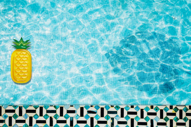 istock Pool floats, rings floating in a refreshing blue swimming pool with palm tree leaf shadows in water 975667032