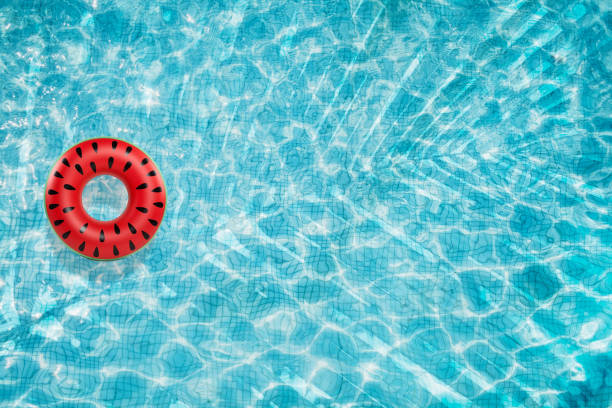 istock Pool floats, rings floating in a refreshing blue swimming pool with palm tree leaf shadows in water 975667158