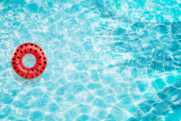 istock Pool floats, rings floating in a refreshing blue swimming pool with palm tree leaf shadows in water 975667344