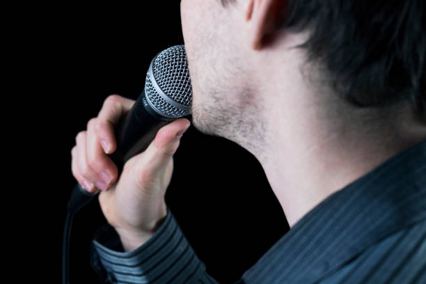 istock Rear view of a man singing to microphone on black background. 975667506