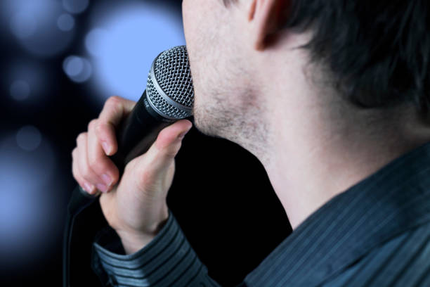 istock Rear view of a man singing to microphone on black background with blurred party lights. 975667532
