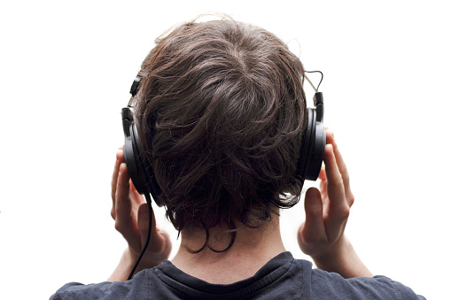 Rear view closeup of young man listening to music with stereo headphones on white background.