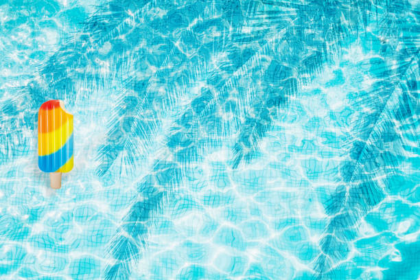 istock Pool floats, rings floating in a refreshing blue swimming pool with palm tree leaf shadows in water 975669920