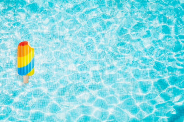 Pool floats, rings floating in a refreshing blue swimming pool with palm tree leaf shadows in water stock photo