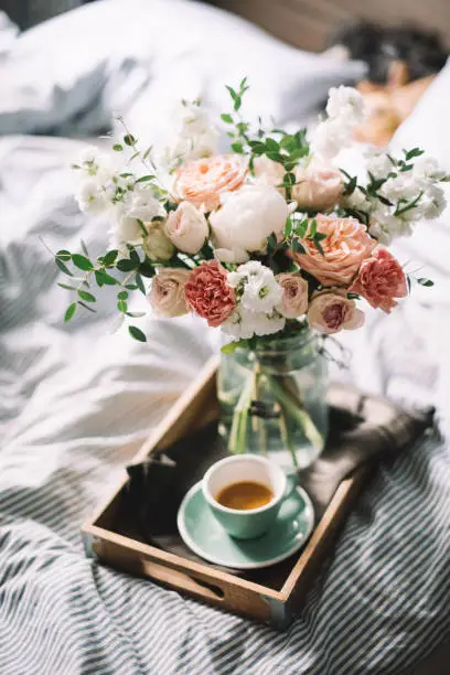 Photo of Delicious fresh morning espresso coffee in bed with a beautiful blossoming flower bouquet of mattiolas, peony, carnations, roses