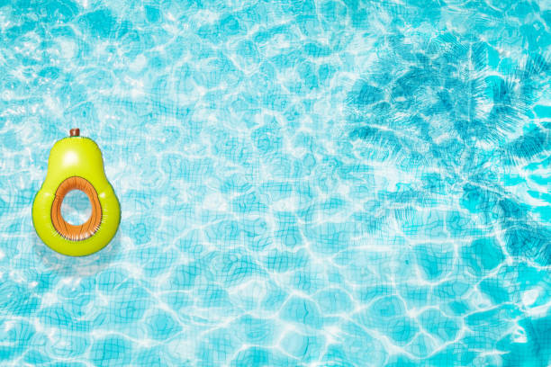 istock Pool floats, rings floating in a refreshing blue swimming pool with palm tree leaf shadows in water 975670474