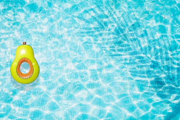 istock Pool floats, rings floating in a refreshing blue swimming pool with palm tree leaf shadows in water 975670508