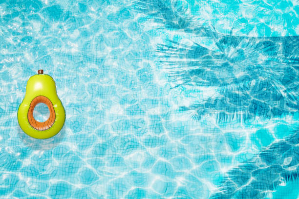 istock Pool floats, rings floating in a refreshing blue swimming pool with palm tree leaf shadows in water 975670516
