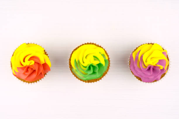 istock Three cupcakes with colorful cream on white wooden table. 975688680