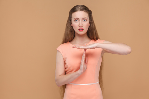 I need more time. please give me timeout. portrait of emotional cute, beautiful woman with makeup and long hair in pink dress. indoor, studio shot, isolated on light brown or beige background.