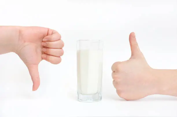 A glass of milk and hands close-up show a sign - like and dislike. Milk is useful and not useful, harmful and not harmful.