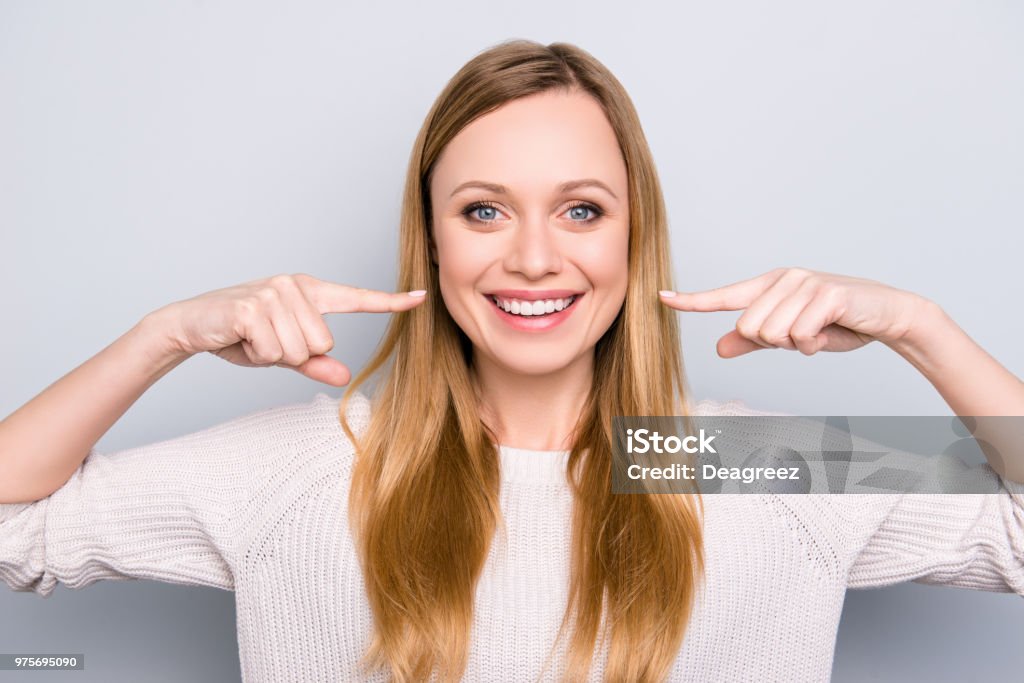 Ritratto di gioiosa ragazza soddisfatta che gesticola i suoi traventi denti bianchi sani con due indice che guardano la fotocamera isolata su sfondo grigio. Concetto ortodontico - Foto stock royalty-free di Sorridere