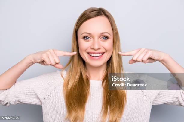 灰色の背景に分離カメラ目線 2 人差し指で彼女の晴れやかな白い健康な歯をジェスチャーうれしそうな満足して女の子の肖像画矯正歯科のコンセプト - 笑顔のストックフォトや画像を多数ご用意