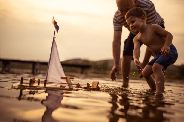 Grandfather and grandson Sailing the boat together Grandfather and grandson playing with a sailboat toy on the lake toy boat stock pictures, royalty-free photos & images