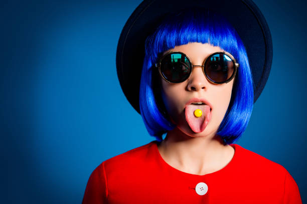 Portrait of childish stupid woman in eyewear head wear gesturing tongue out with small yellow candy isolated on blue background. Confecrtionery sweets concept Portrait of childish stupid woman in eyewear head wear gesturing tongue out with small yellow candy isolated on blue background. Confecrtionery sweets concept angry hairstylist stock pictures, royalty-free photos & images