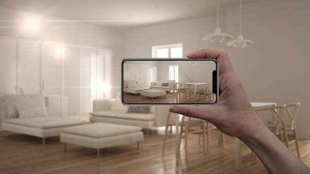 istock Hand holding smart phone, AR application, simulate furniture and interior design products in real home, architect designer concept, blur background, modern living room with kitchen 975701316