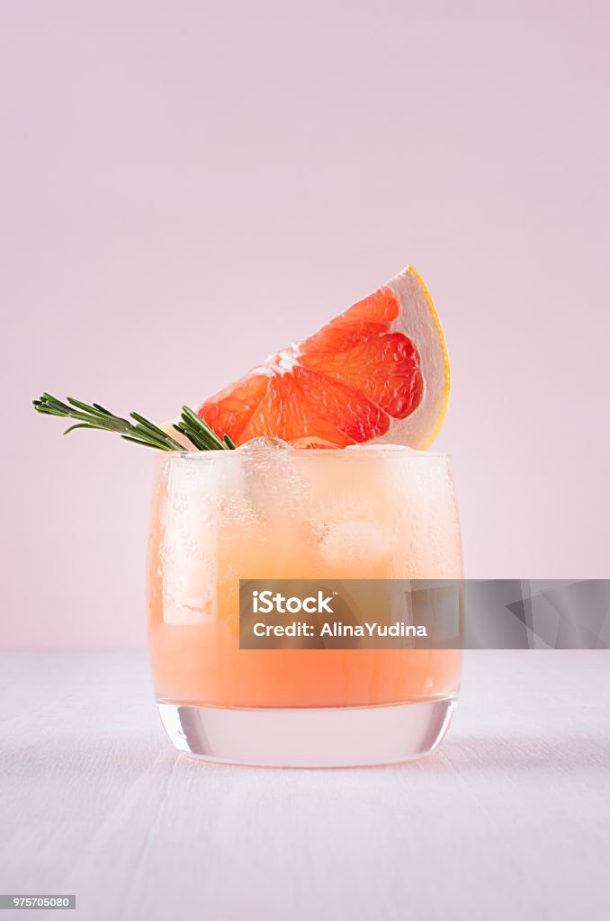 Cold detox cocktail of grapefruit juice with ice, rosemary, slices citrus on soft light pink and white background. Cocktail Stock Photo