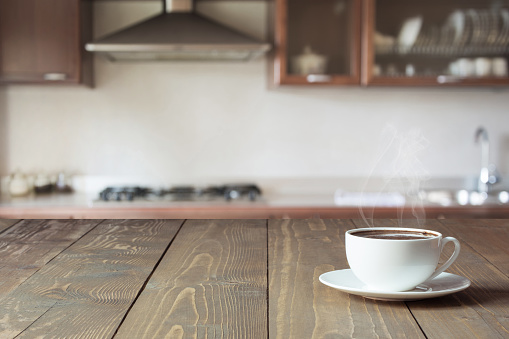 Cup of black coffee on wooden tabletop in blurred modern kitchen. Close up. Indoors.