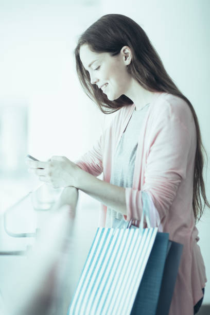 istock Smiling young woman using smartphone in mall 975713162