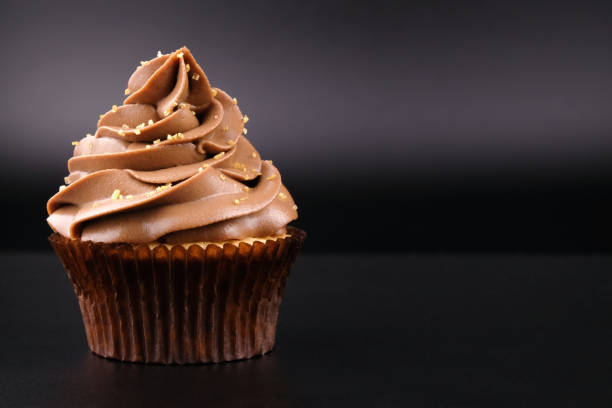 istock Cupcake with whipped chocolate cream, decorated, gold confectionery sprinkling on black background. 975729514