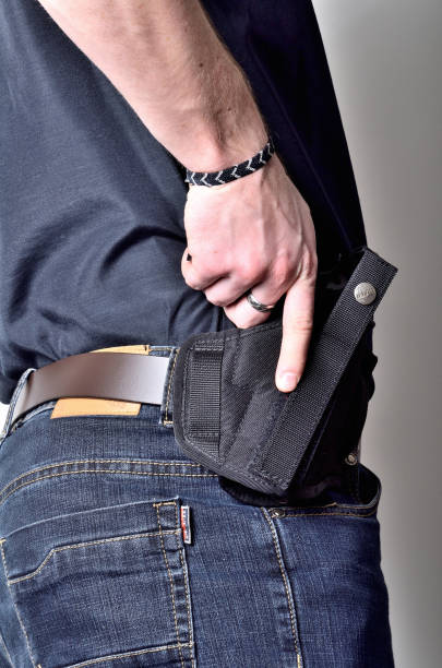 istock Man pulling out a pistol gun from the holster on belt, blue jeans, black shirt 975730118