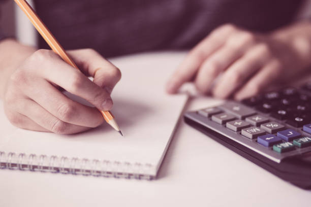 istock Closeup of Hands Using Calculator and Writing 975735834