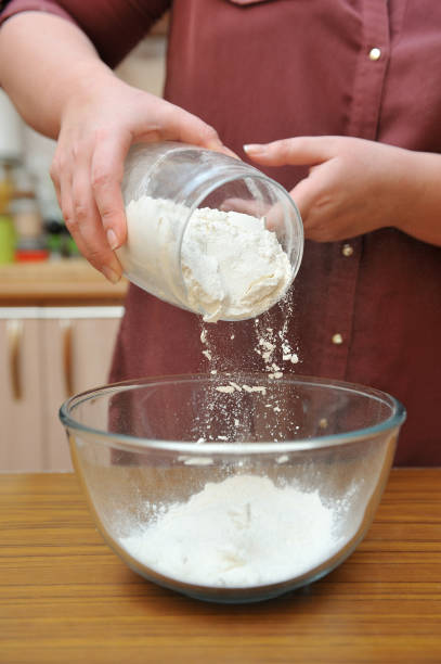 istock Female hands pour wheat flour into a glass bowl on a table 975742684