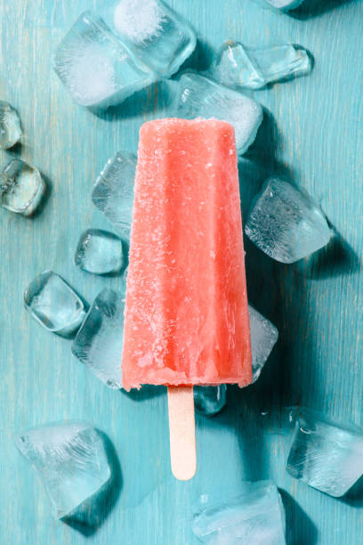 istock Red fruit ice pop on wooden background with ice cubes 975753928