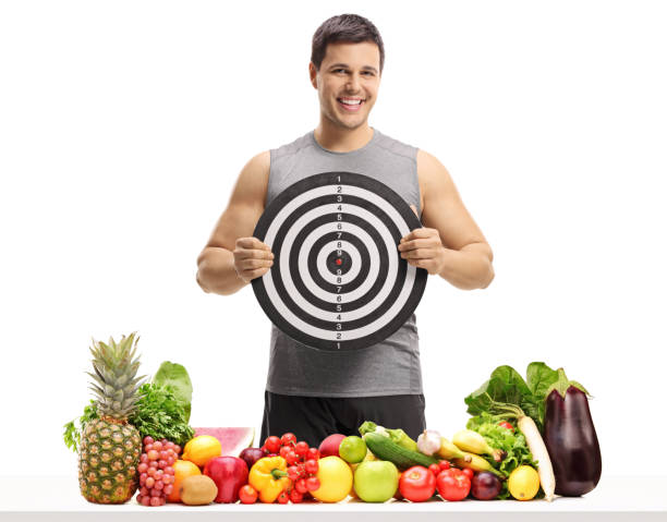 hombre joven detrás de una mesa con frutas y verduras con un objetivo - dartboard photography competition sports and fitness fotografías e imágenes de stock