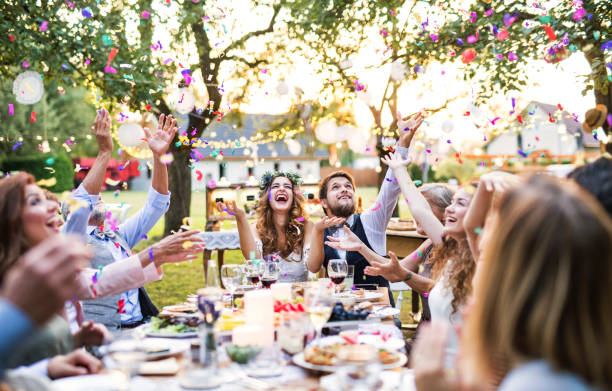 Bride and groom with guests at wedding reception outside in the backyard. Wedding reception outside in the backyard. Bride and groom with family and guests sitting around the table, having fun. wedding stock pictures, royalty-free photos & images