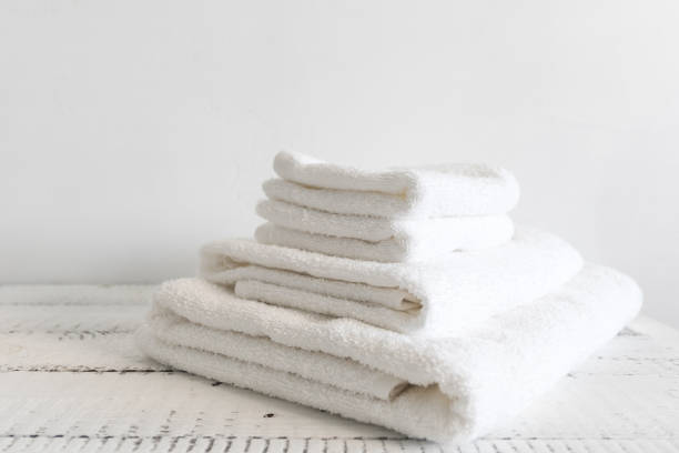 istock Folded white bath towels on white wooden table. Spa and wellness, cotton terry textile. 975842990