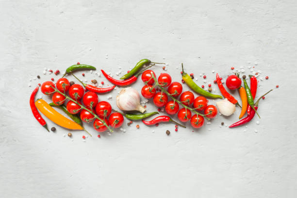 istock Hot chili peppers multi-colored, tomato cherry on branch, garlic and other spices on grey background Copy space 975845548