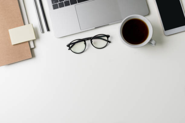 istock Top view of office workplace. White desk with copy space. Flat lay view on table with laptop, phone, notebooks, glasses, memo pads, cup of coffee and pens. Creative designer concept. 975845794