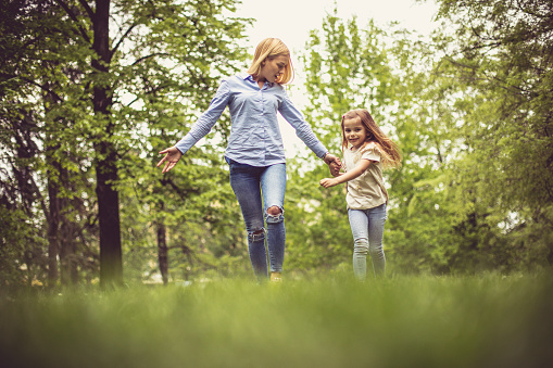 Mother and daughter in park running and holding hands.