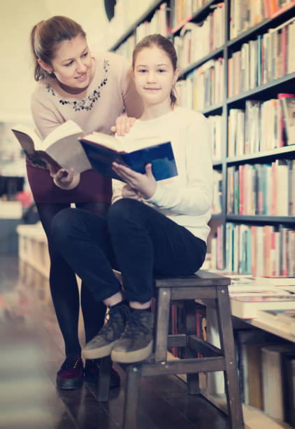 istock Glad girl choosing interesting book with mother 975847974
